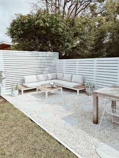 an outdoor seating area in the middle of a yard with white walls and wooden furniture