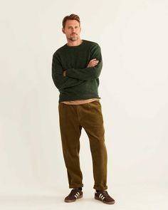 a man standing with his arms crossed in front of him, wearing green sweater and khaki pants