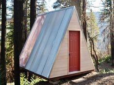 a tiny house in the woods with a red door and metal shingles on it