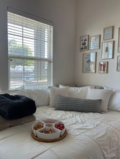 a bed with white sheets and pillows in front of a window filled with framed pictures