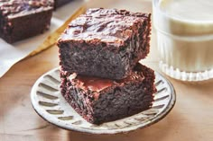 three chocolate brownies on a plate next to a glass of milk