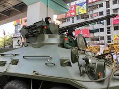 an army tank is parked in front of a building and people are standing around it