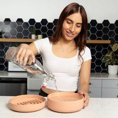 a woman pouring something into a bowl on top of a counter