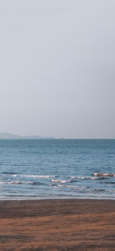 a person walking on the beach with a surfboard in their hand and an island in the distance