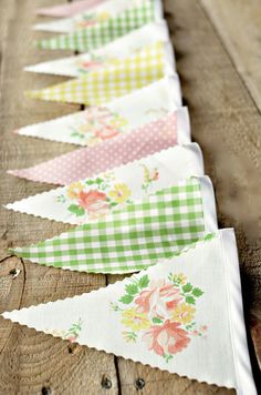 several bunting flags are lined up on a wooden table with flowers and gingham