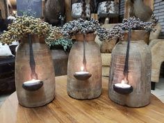 three vases sitting on top of a wooden table filled with flowers and lit candles