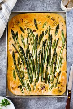 asparagus on top of bread in a baking pan with knife and bowl next to it