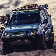 a black suv parked on top of a dirt hill next to a tree with clouds in the background