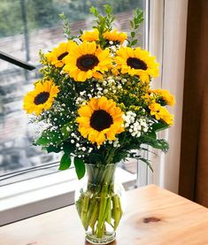 a vase filled with yellow sunflowers sitting on top of a table next to a window