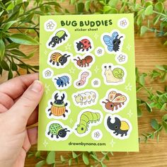 a hand holding a green sticker sheet with bugs and insects on it next to some plants