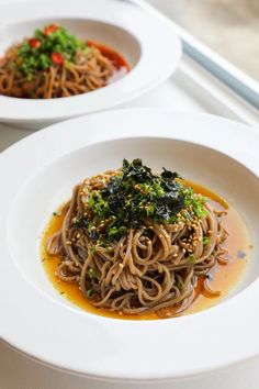 two white plates filled with noodles and vegetables on a table next to a window sill