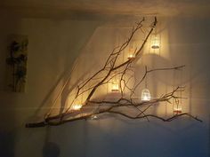 a tree branch with candles on it and some branches hanging from the wall in front of it