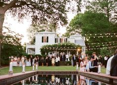 a group of people standing in front of a pool surrounded by trees and string lights