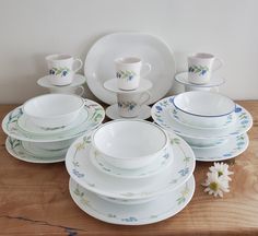 a wooden table topped with lots of white plates and bowls filled with flowers next to each other