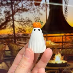 a hand holding a small white ghost figurine in front of a fire pit