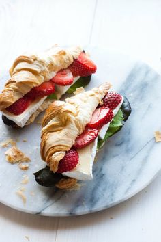 two croissants with strawberries and cream cheese on them sitting on a marble plate