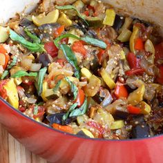 a red pot filled with cooked vegetables on top of a wooden cutting board next to a knife