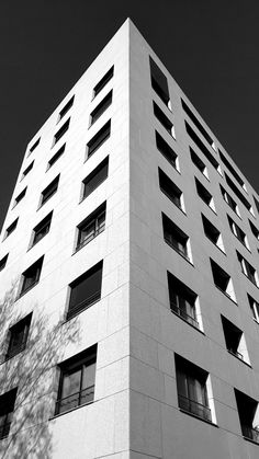 black and white photograph of a tall building with windows on the top floor, in front of a tree