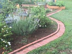 a garden with brick edging and flowers in the foreground, surrounded by green grass