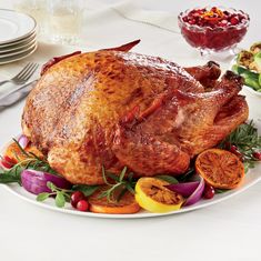 a roasted turkey on a platter with oranges, cranberries and other holiday foods