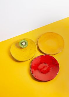 three plates sitting on top of a yellow table next to a green kiwi slice