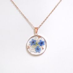 a necklace with blue and white flowers in the center on a gold plated chain