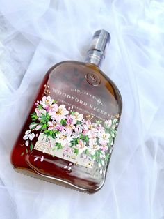 a bottle of liquor sitting on top of a white cloth covered tablecloth with flowers painted on it