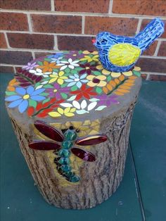 two birds sitting on top of a tree stump with flowers and butterflies painted on it