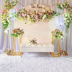 an arrangement of flowers and greenery is displayed on a white backdrop with gold stand