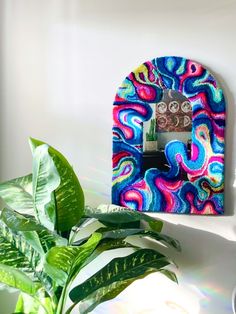 a colorful wall mounted phone on a white shelf next to a green potted plant