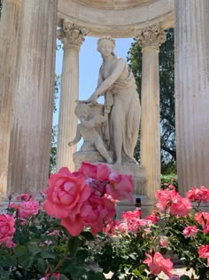 the statue is surrounded by pink flowers in front of some stone pillars and arches with columns on either side