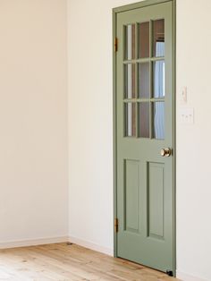 an empty room with a green door and white walls, hardwood flooring is in the foreground