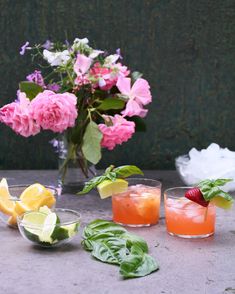 three glasses filled with different types of drinks next to pink flowers and green leaves on a table