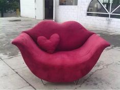 a heart shaped chair sitting on the ground in front of a white building with windows