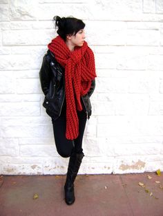 a woman standing against a white brick wall wearing a red scarf and black leather jacket