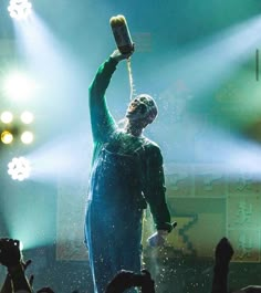 a man in blue jumpsuit holding up a cell phone while standing on stage surrounded by people