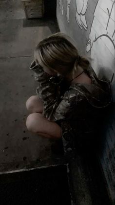 a young woman sitting on the ground next to a wall with graffiti painted on it