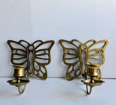 two brass butterfly wall sconces with candle holders on each side, one has a light bulb in the middle