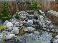 a garden with rocks and water features a small waterfall in the center, surrounded by greenery