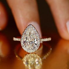 a woman's hand holding an engagement ring with a pear shaped diamond