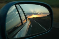 the side view mirror of a car is shown as the sun sets in the distance