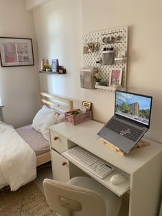 a laptop computer sitting on top of a white desk next to a bed and chair