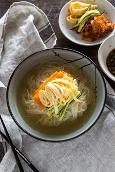 two bowls filled with noodles and vegetables next to chopsticks on a table top