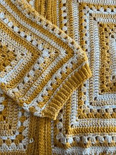 a crocheted yellow and white blanket is laying on top of each other,