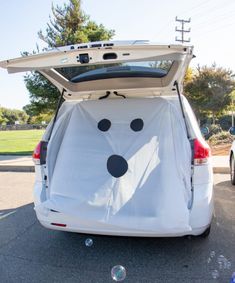 the back end of a white car with its trunk open and it's face painted like a dog