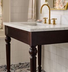 a bathroom sink sitting under a mirror next to a wooden stand with two faucets