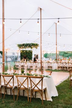 an outdoor tent with tables and chairs set up for a wedding reception at night time