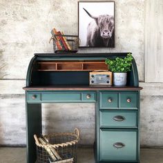 an old desk with a cow painting on the wall above it and a basket next to it