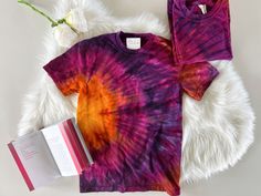 a purple and orange tie dye shirt next to a book on a white fur rug