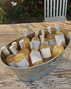 several bottles of liquid sitting in a bucket on a wooden table with white chairs behind them